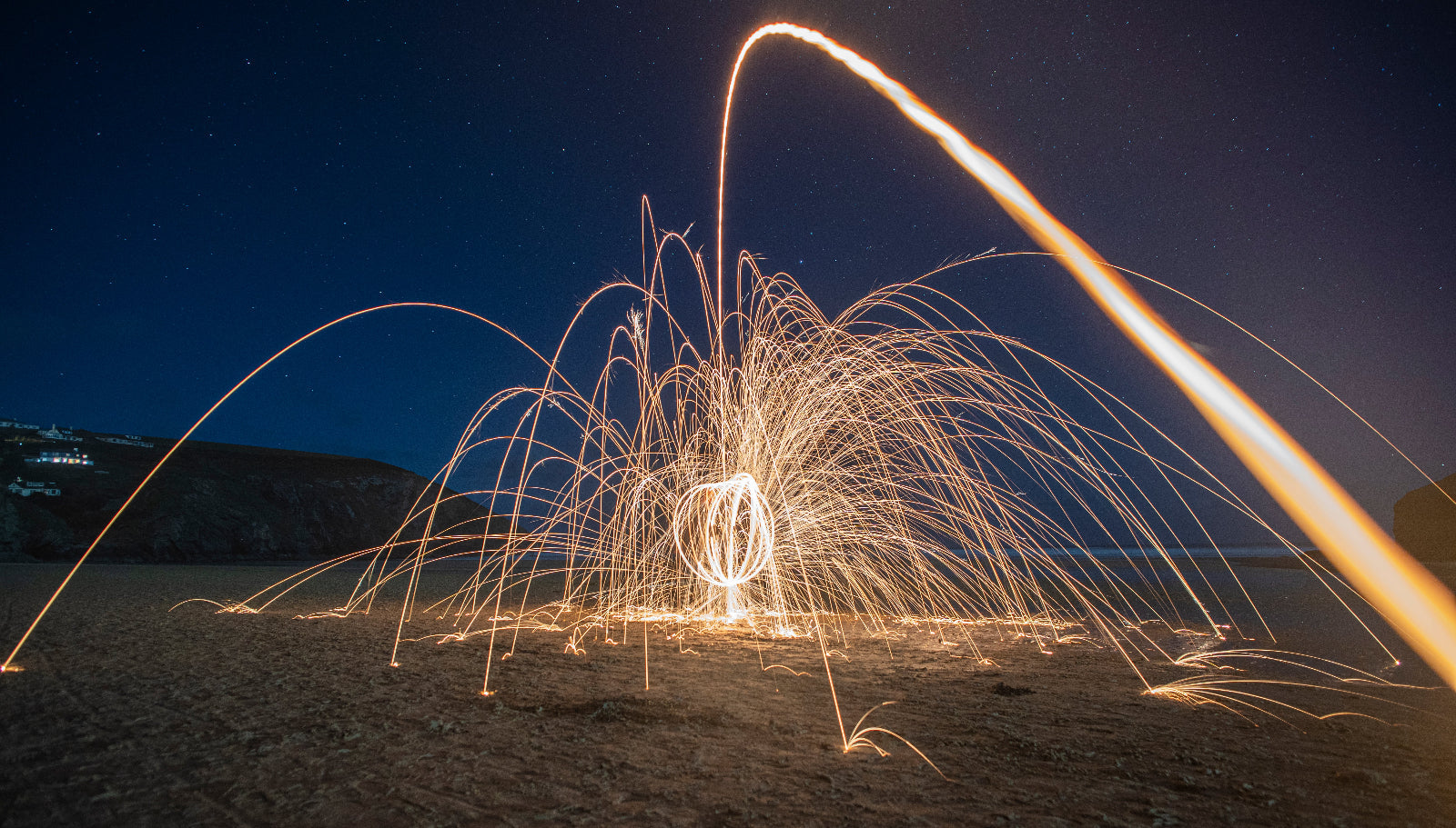 Sparks from steel wool on a beach at night with a dark blue sky.