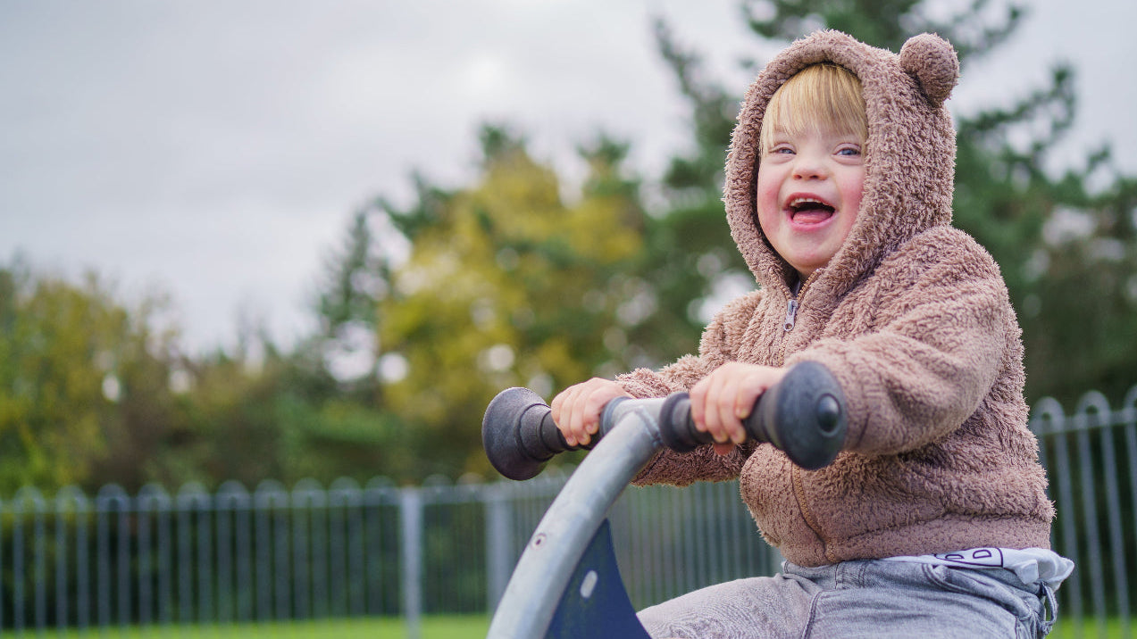 Child wearing a bear-themed hoodie on a playground ride with trees in the background